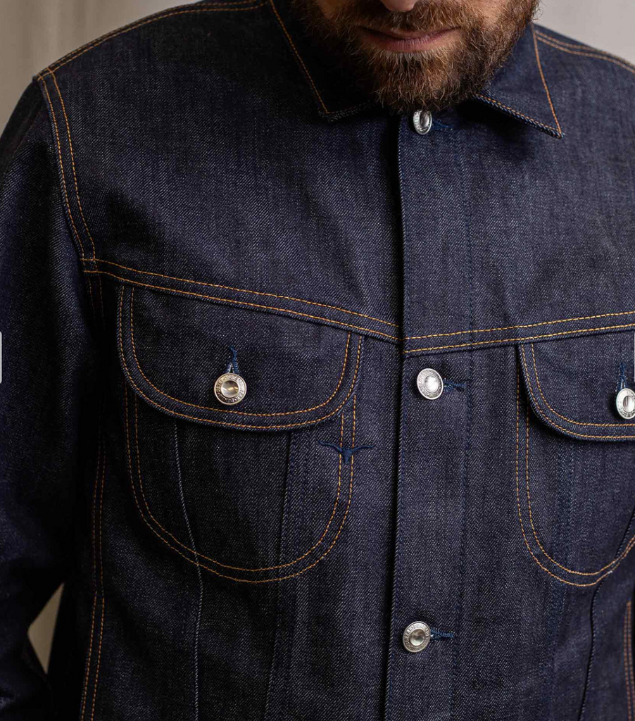 Slim-fit trucker jacket made from raw 15 oz. Italian selvedge denim with chest, hand-warmer, and inside pockets, showcasing vintage style.