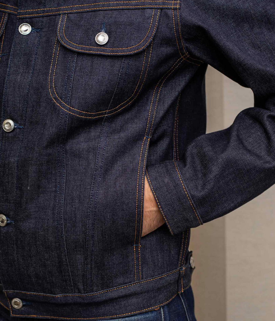 Slim-fit trucker jacket made from raw 15 oz. Italian selvedge denim with chest, hand-warmer, and inside pockets, showcasing vintage style.