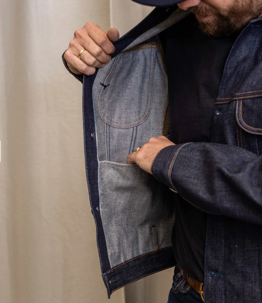 Slim-fit trucker jacket made from raw 15 oz. Italian selvedge denim with chest, hand-warmer, and inside pockets, showcasing vintage style.