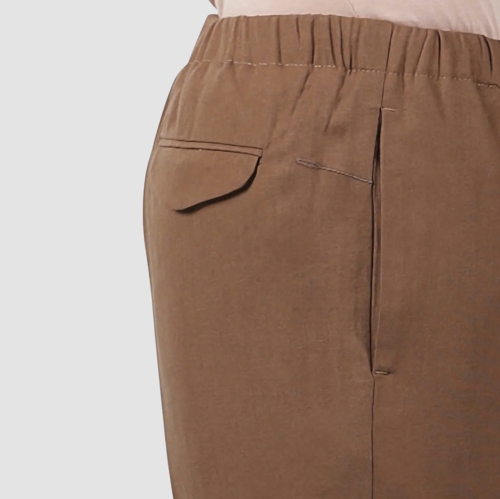 A pair of loose-fit trousers in a soft linen-blend fabric, featuring an elastic waistband, front pockets, and back pockets with flaps.