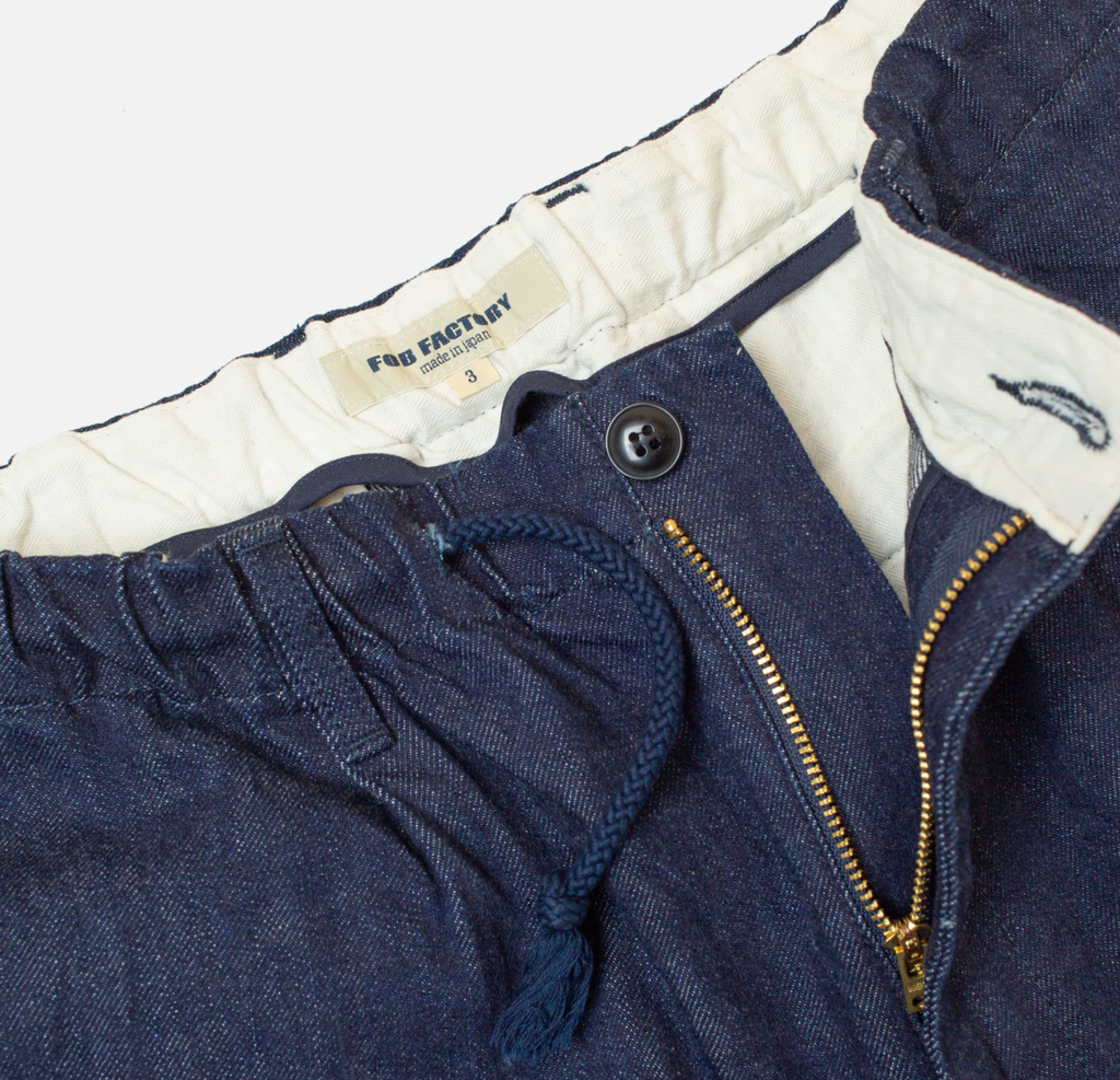 Close up of a pair of denim chinos on a light grey background. 