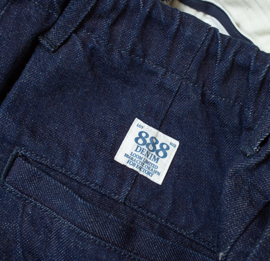 Close up of a pair of denim chinos on a light grey background. 