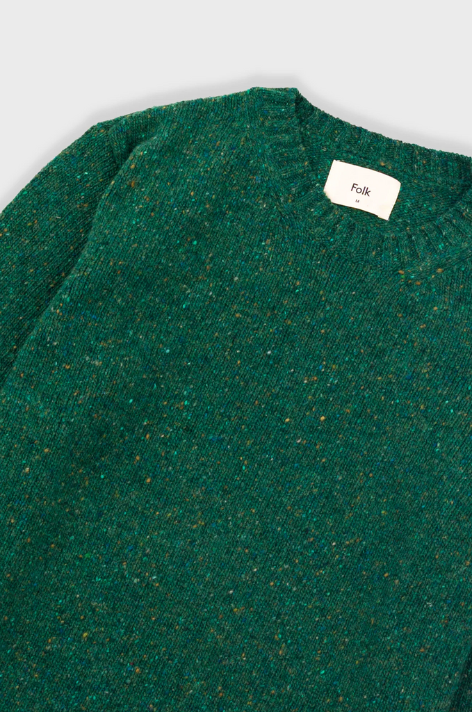 Green textured sweater with a brand label on a light gray background.