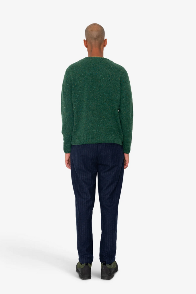 Person wearing a green sweater and dark pants on a white background.