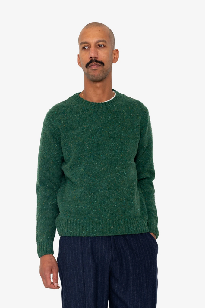 Man wearing a green sweater and dark pants on a white background.