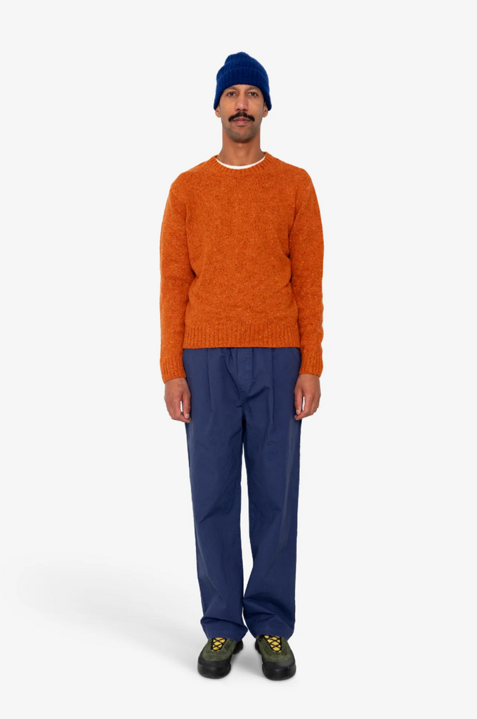 Man wearing an orange sweater and blue pants on a white background.