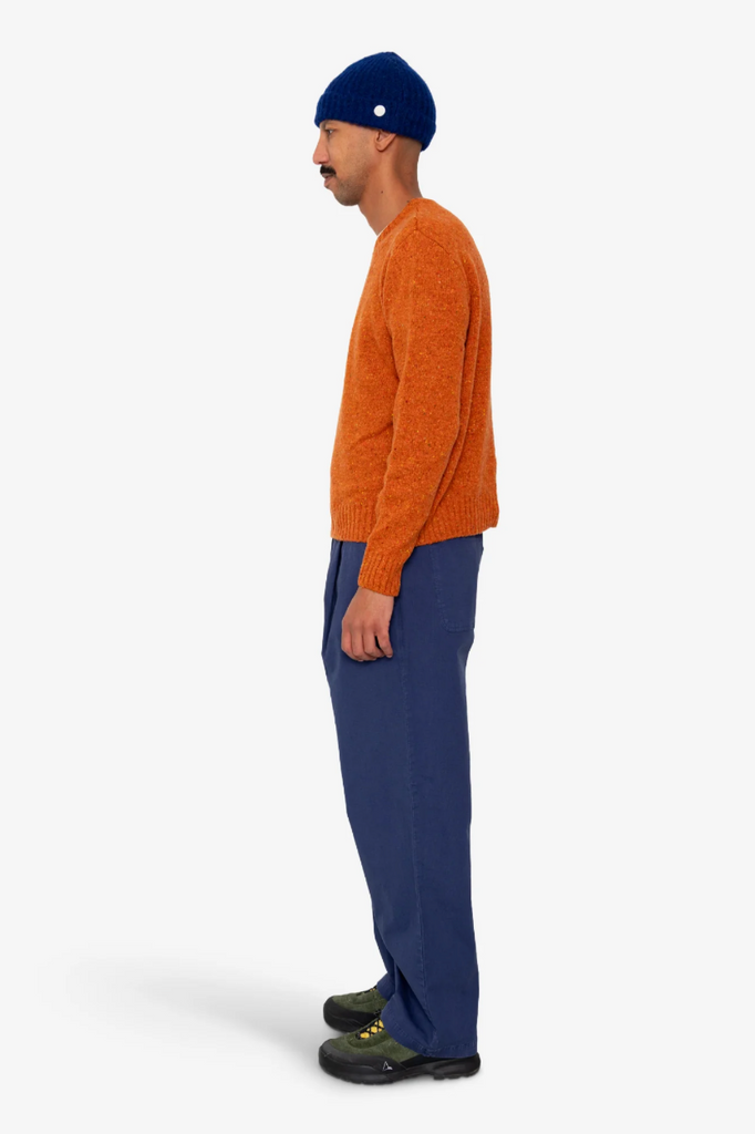 Person wearing an orange sweater and blue pants on a white background.