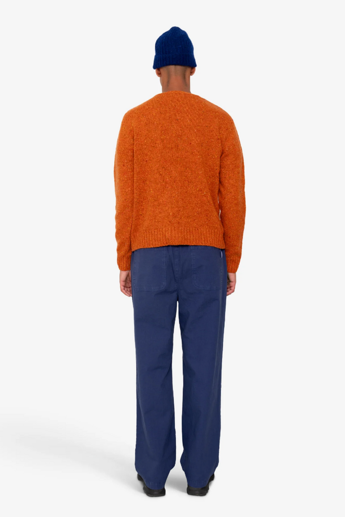 Person wearing an orange sweater and blue pants on a white background.