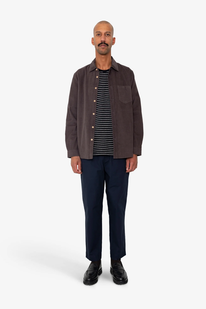 Man wearing a purple shirt, striped tshirt, and dark pants on a white background