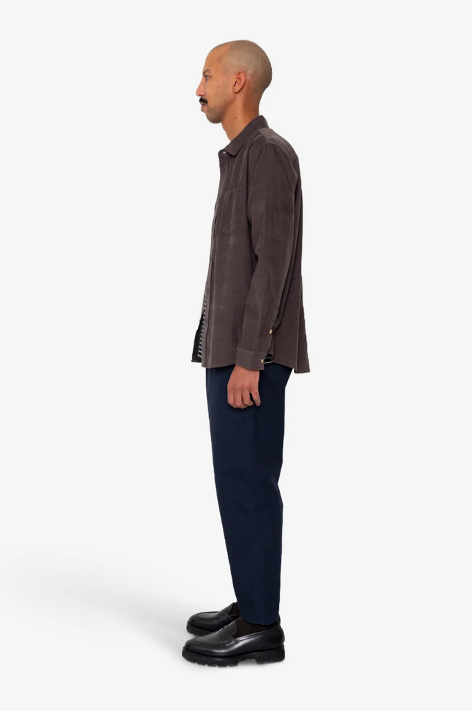 Man wearing a purple shirt and dark pants on a white background.
