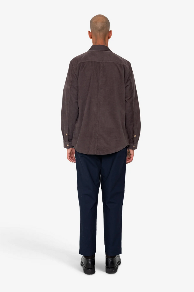 Man wearing a purple shirt and dark pants on a white background.