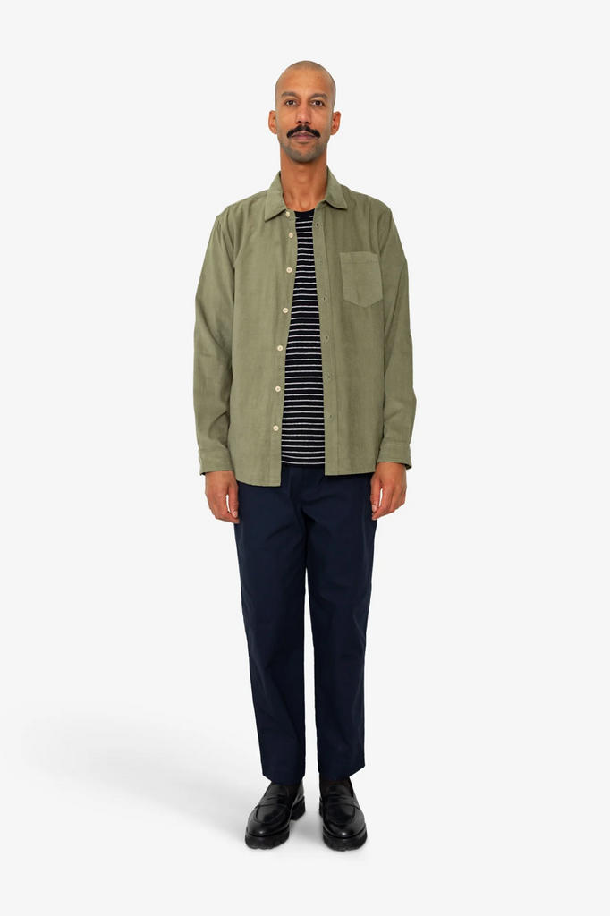 Man wearing a green jacket, striped shirt, and dark pants on a white background.