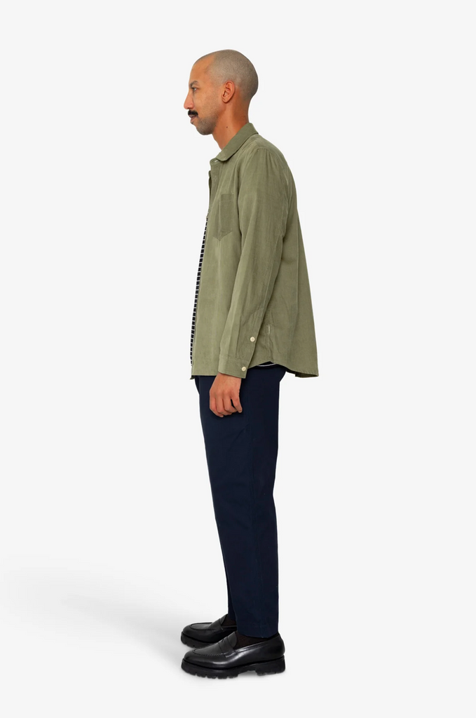 Man wearing a green jacket and dark pants on a white background.