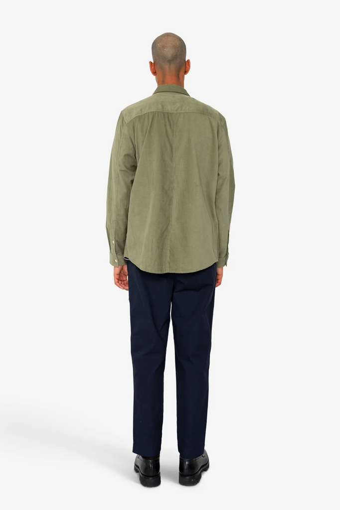 Man wearing a green shirt and dark pants on a white background.