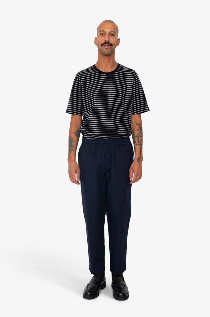 Man wearing a black and white striped shirt and navy pants on a white background.