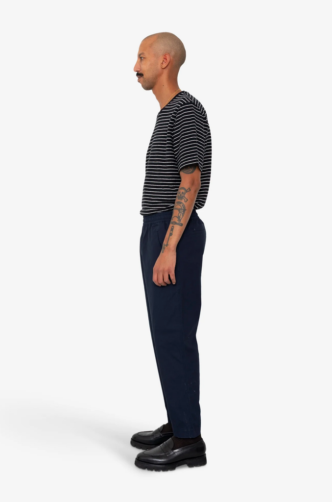 Man wearing a striped shirt and dark pants on a white background.
