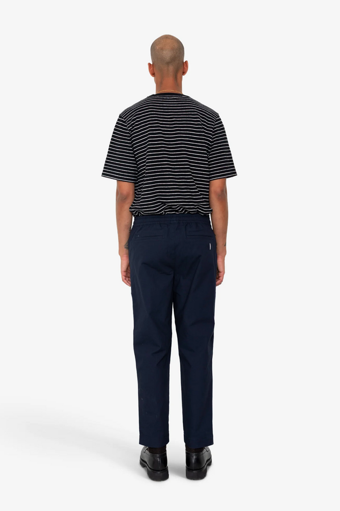 Person wearing a black and white striped shirt and navy pants on a white background.