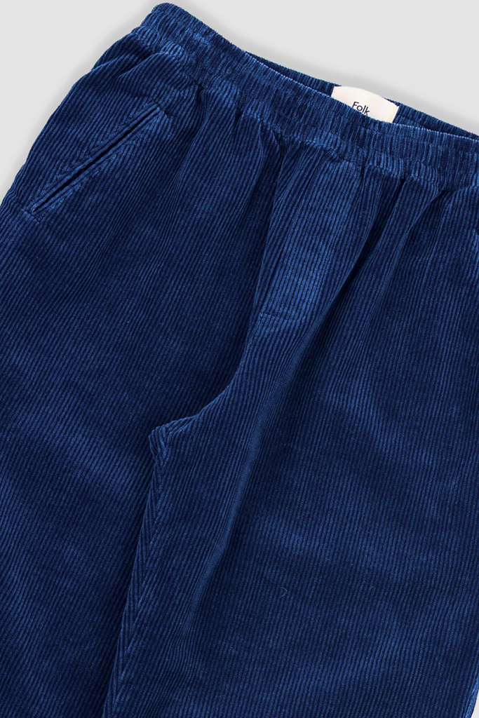 Close-up of blue corduroy pants with a visible brand label on a light gray background.
