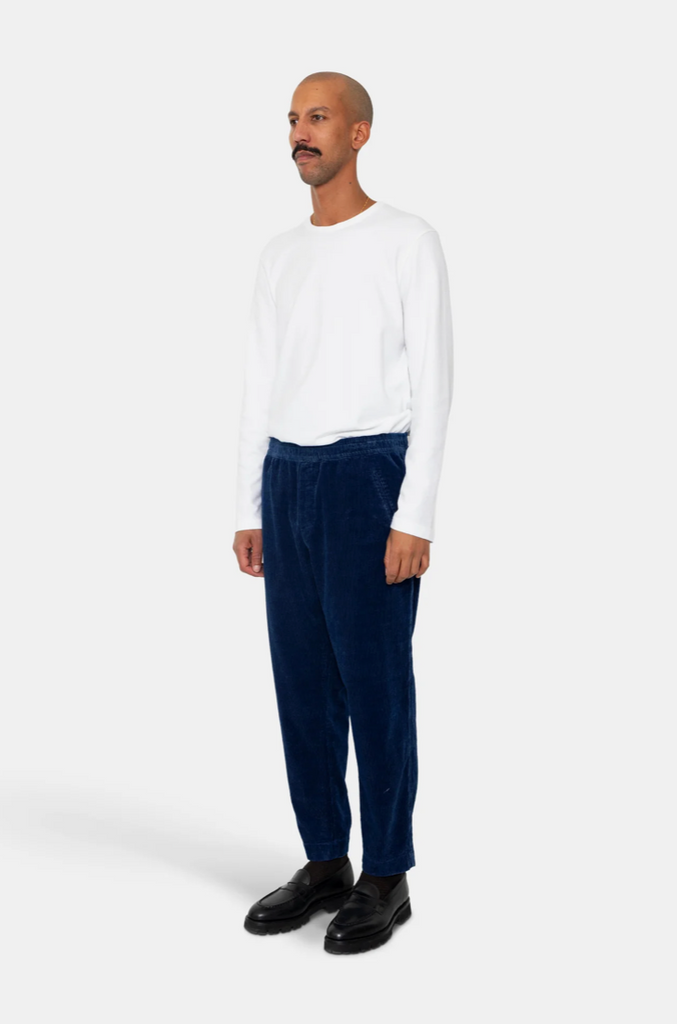 Man wearing white t-shirt and blue corduroy elasticated waistband pants on a grey background.