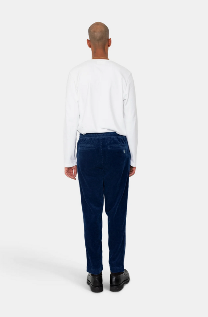Man wearing white t-shirt and blue corduroy elasticated waistband pants on a grey background.