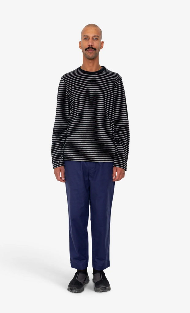 Man wearing a black and white striped sweater and blue pants on a white background.
