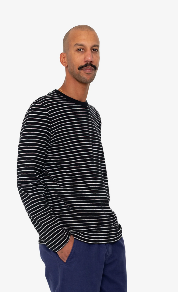 Man wearing a black and white striped long-sleeve shirt and blue pants on a white background.