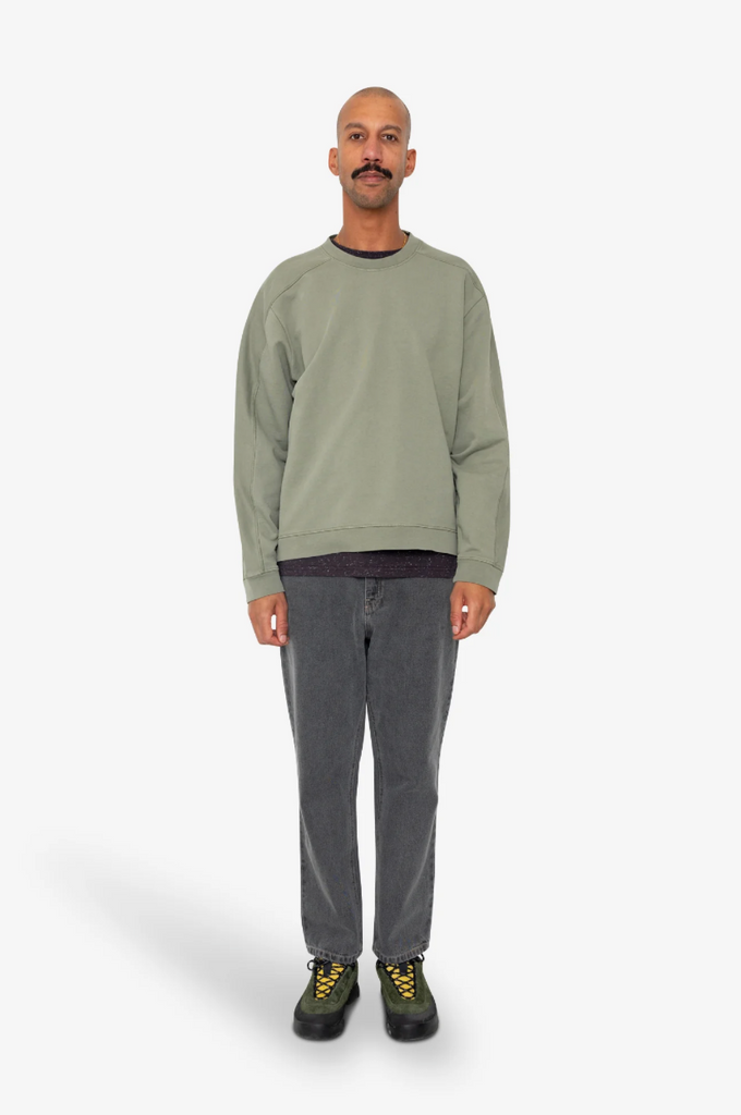 Man wearing a green sweatshirt and gray pants on a white background.