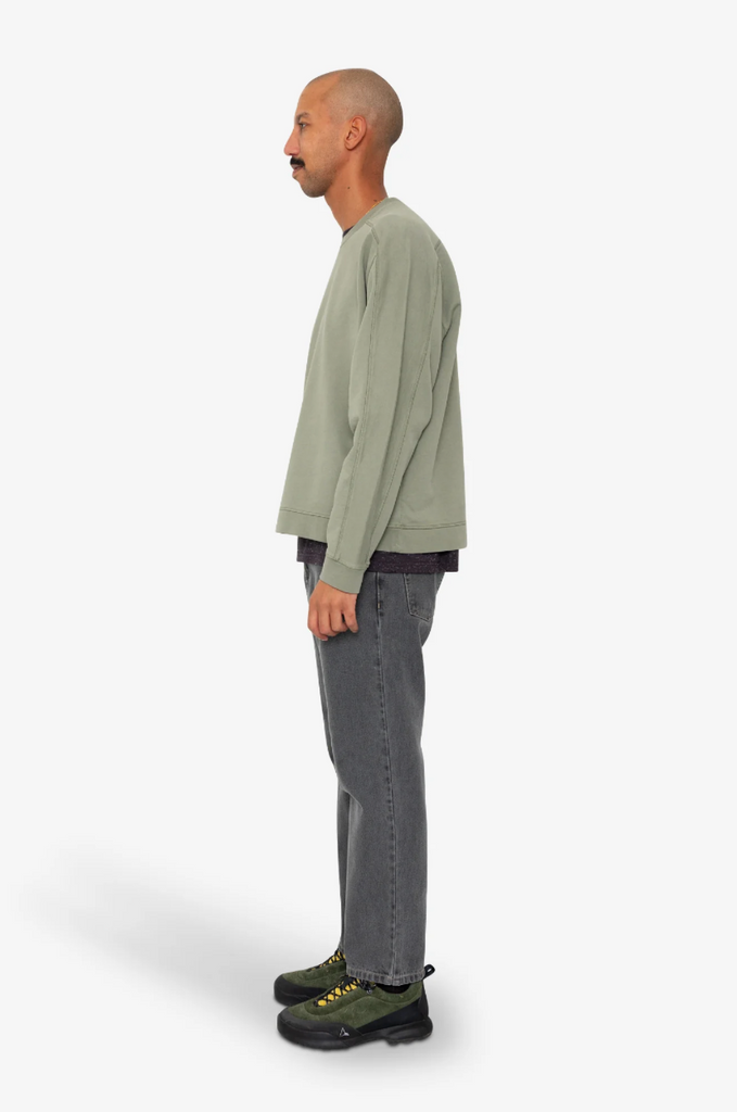 Man wearing a green sweater and gray pants standing against a white background.