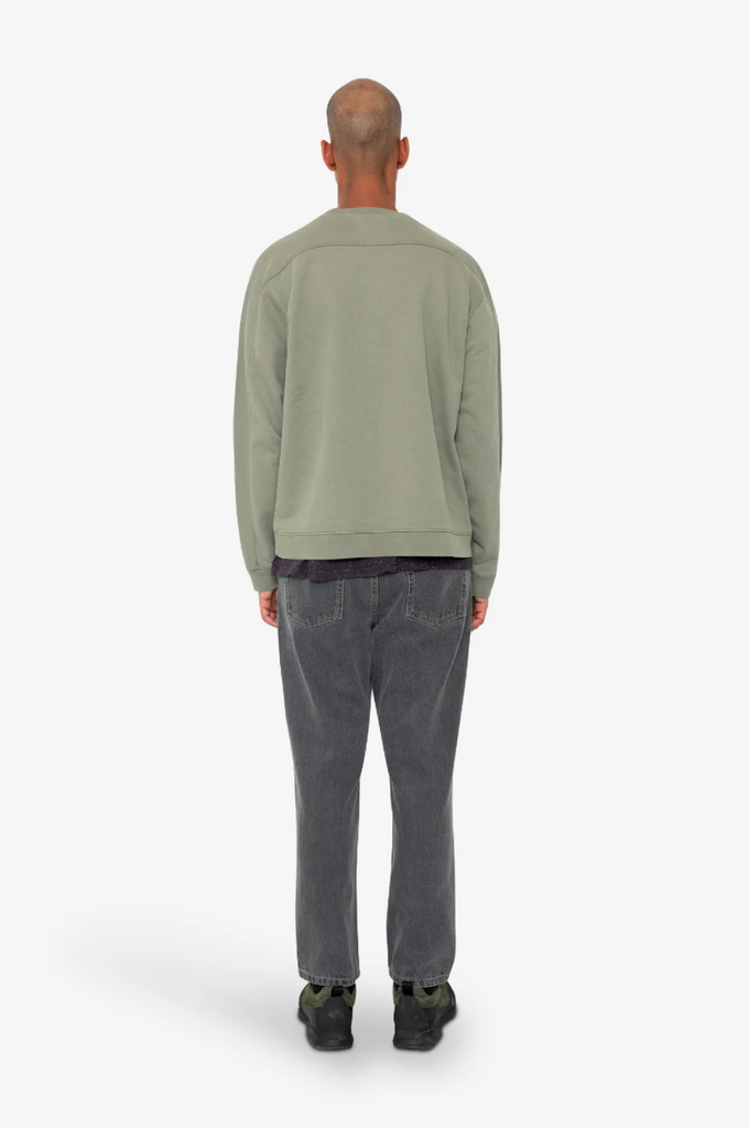 Person wearing a green sweater and gray pants on a white background.