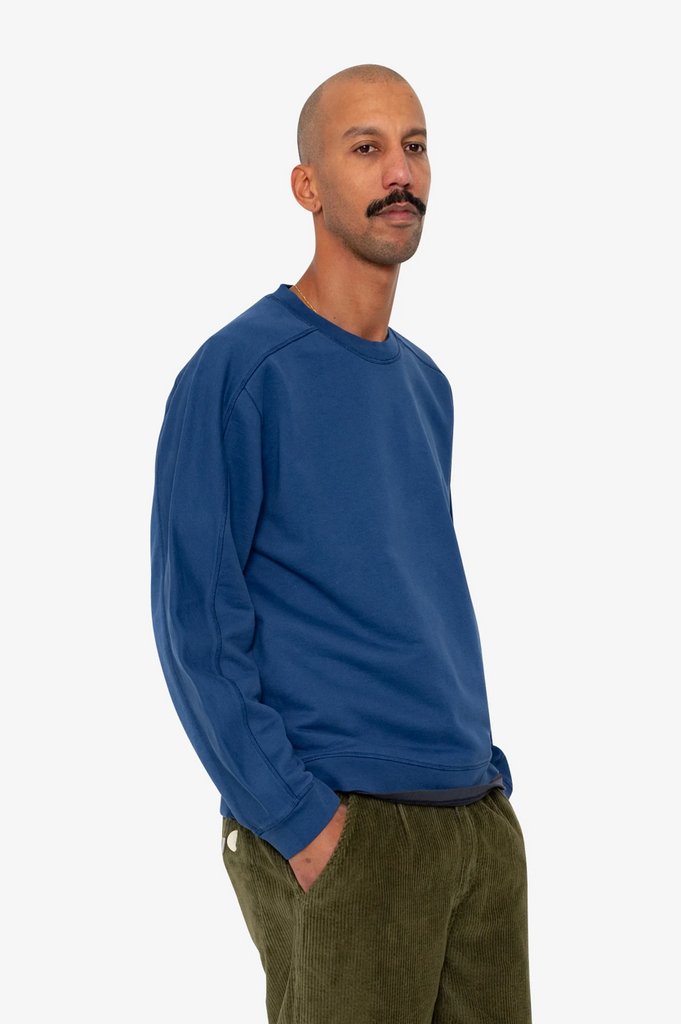 Man wearing a blue sweatshirt and green pants on a white background.