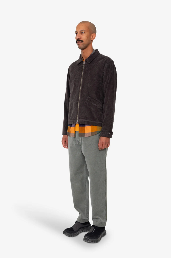 Man wearing a dark corduroy jacket, plaid shirt, and gray pants on a white background.