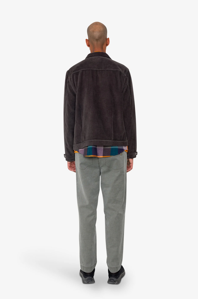 Man wearing a dark corduroy jacket and gray pants on a white background.