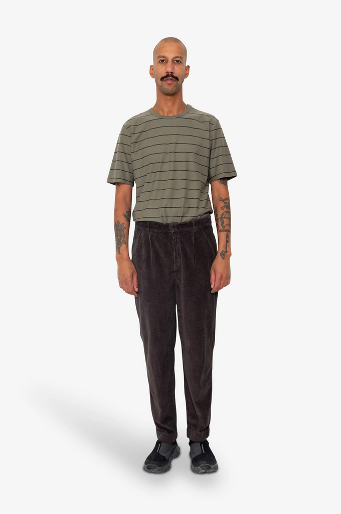 Man wearing a striped shirt and brown corduroy pants on a white background.