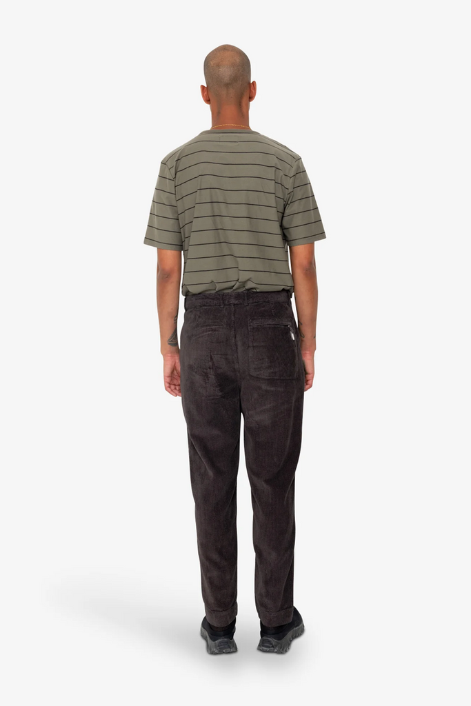 Man wearing a striped shirt and dark corduroy pants on a white background.