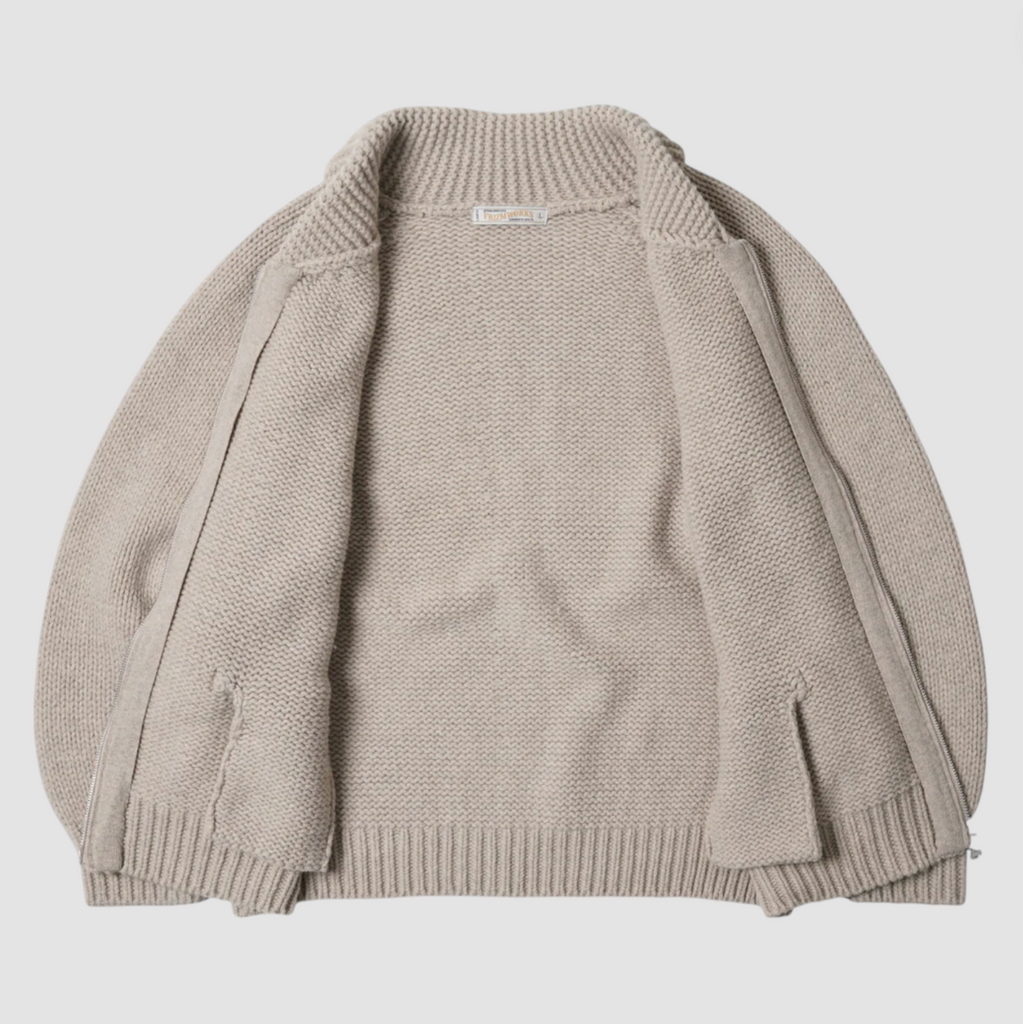 Beige knitted zip up sweater on a light gray background.