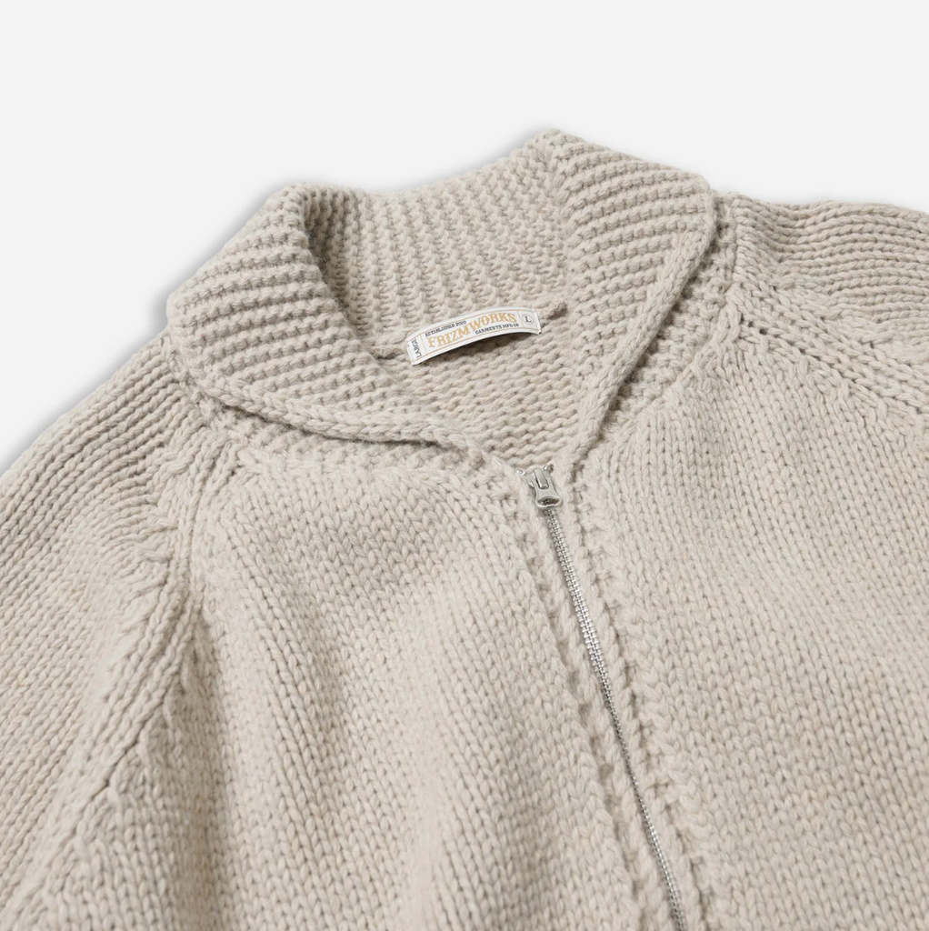 Close-up of a beige knit sweater with a zipper on a light gray background.