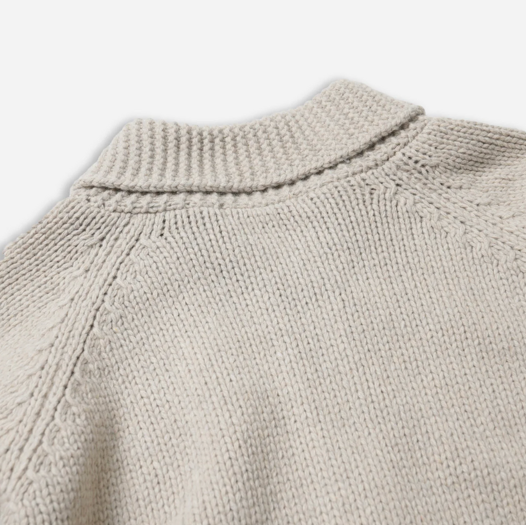 Close-up of a beige knitted sweater collar on a light gray background.