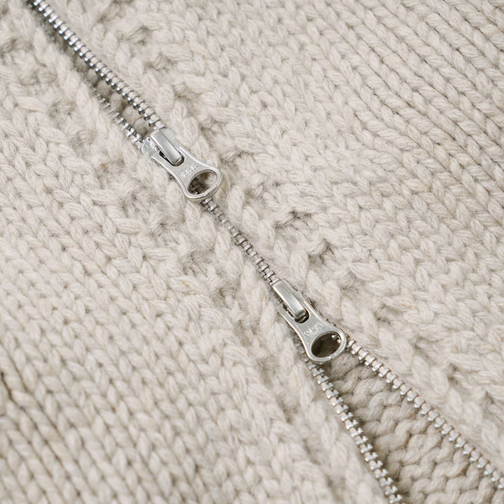 Close-up of a silver zipper on a textured beige knitted fabric.