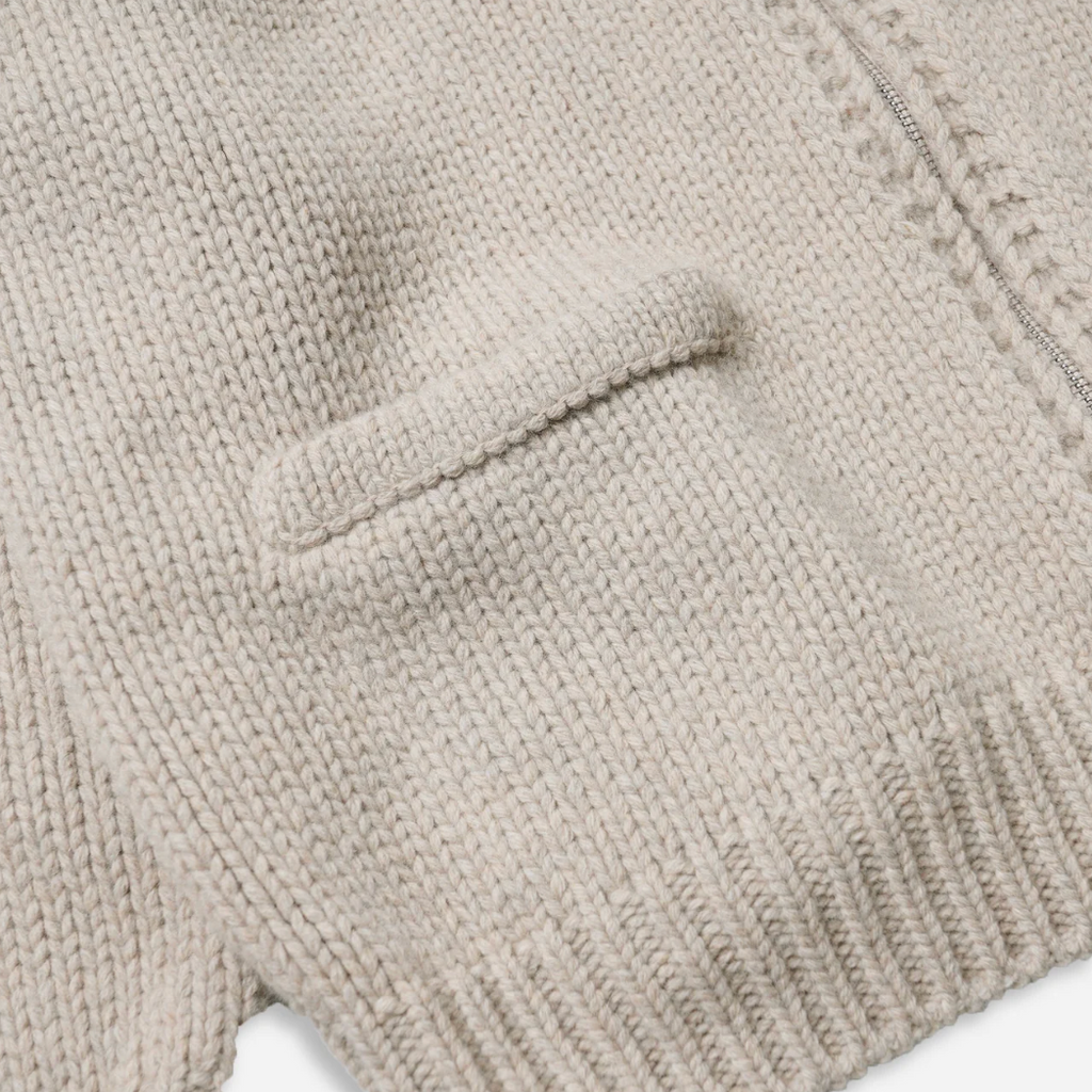 Close-up of a beige knitted sweater with a pocket on a white background.