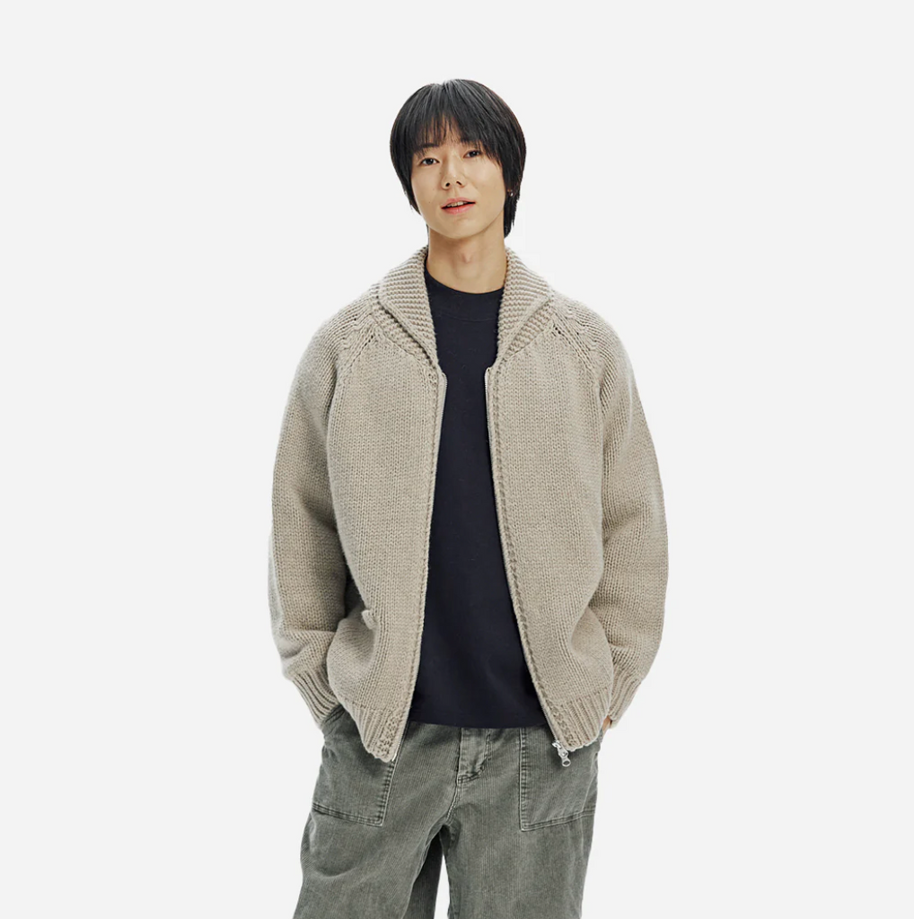 Person wearing a beige knitted zip up cardigan on a white background.