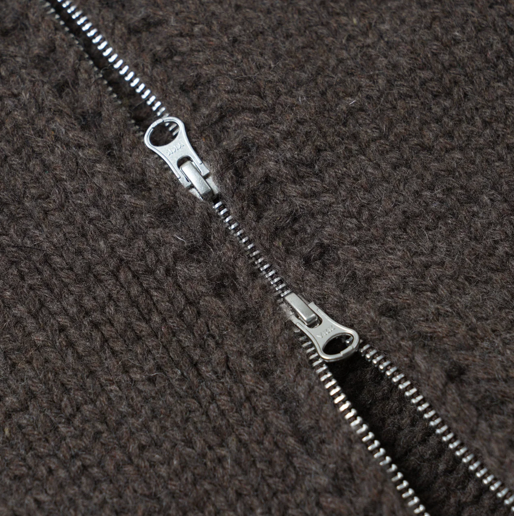 Metal zipper partially unzipped on a textured brown knitted fabric background.