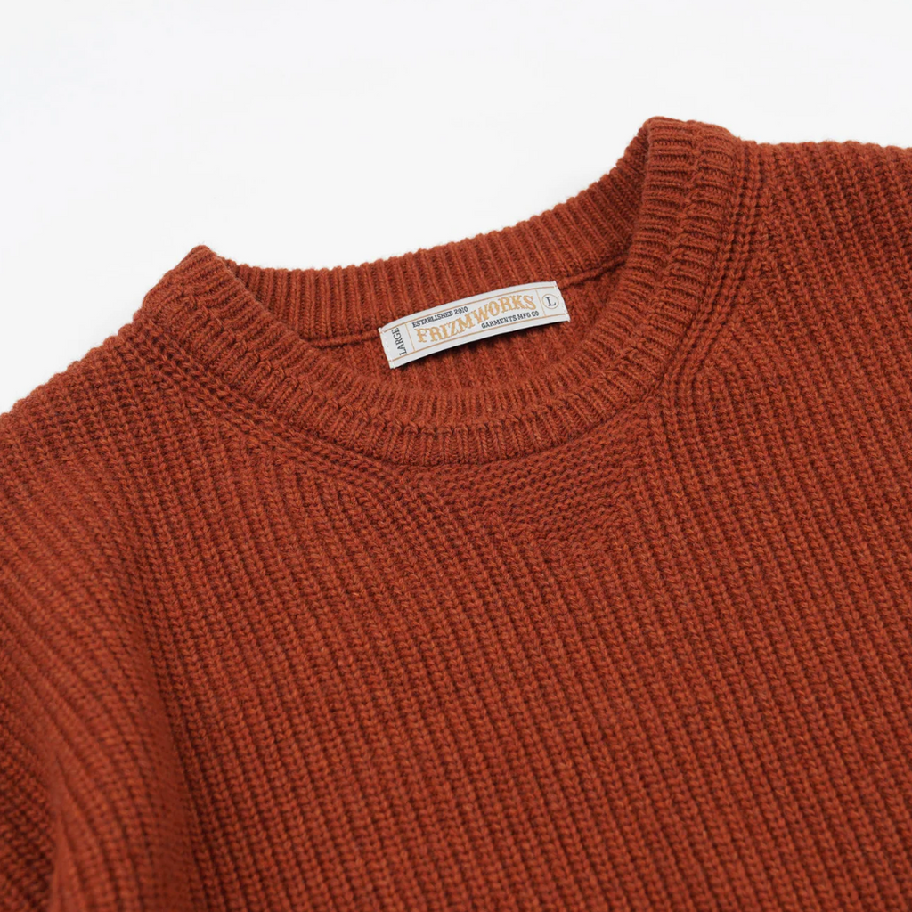 Close-up of an orange sweater with a brand label on a white background.