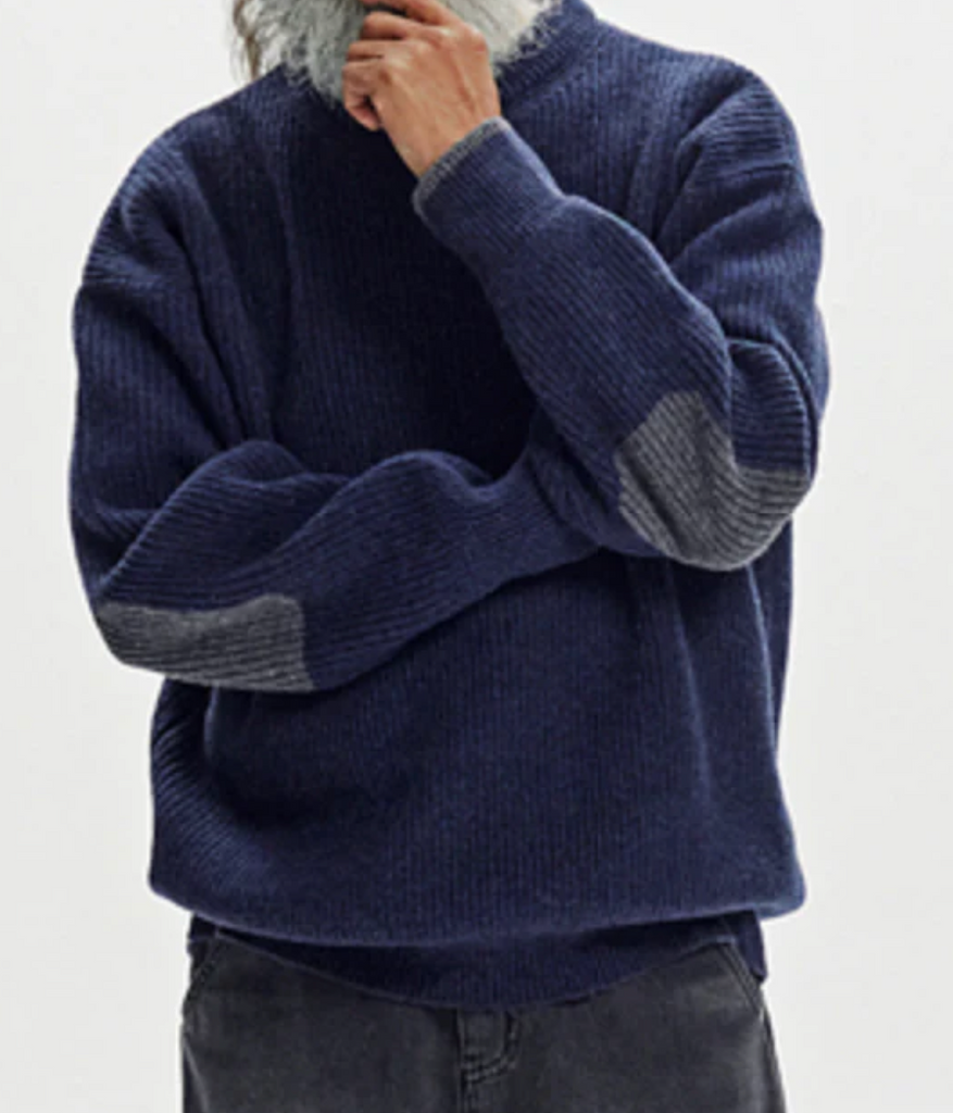 Person wearing a blue sweater with grey elbows, and cuffs on a white background.