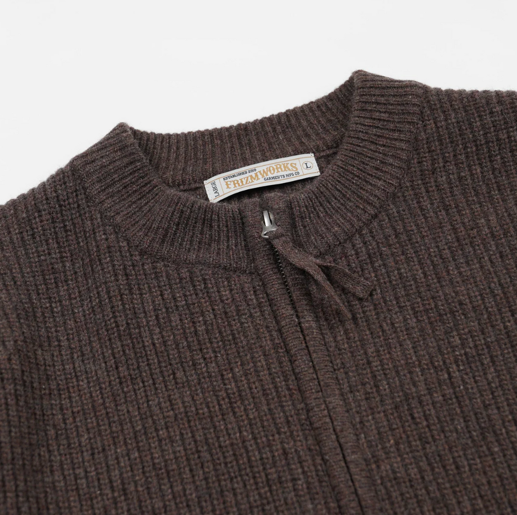 Close-up of a brown knit zip up sweater with a brand label on a white background.