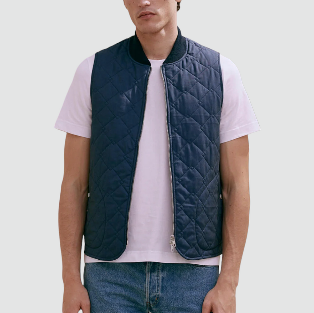 A navy quilted bomber gilet with a zip fastening, ribbed collar, cross diamond pattern, large welt pockets, and lightweight cotton fabric.