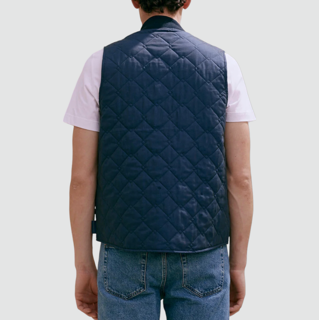 A navy quilted bomber gilet with a zip fastening, ribbed collar, cross diamond pattern, large welt pockets, and lightweight cotton fabric.