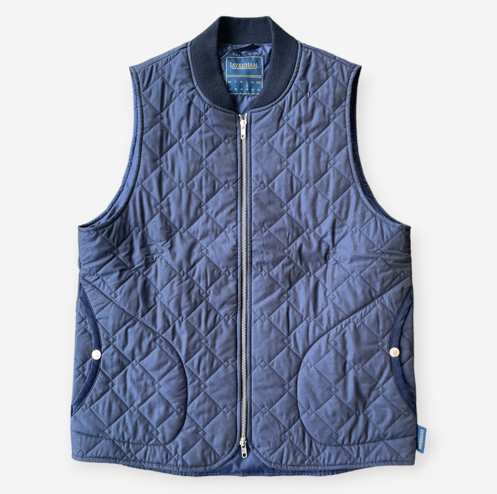 A navy quilted bomber gilet with a zip fastening, ribbed collar, cross diamond pattern, large welt pockets, and lightweight cotton fabric.