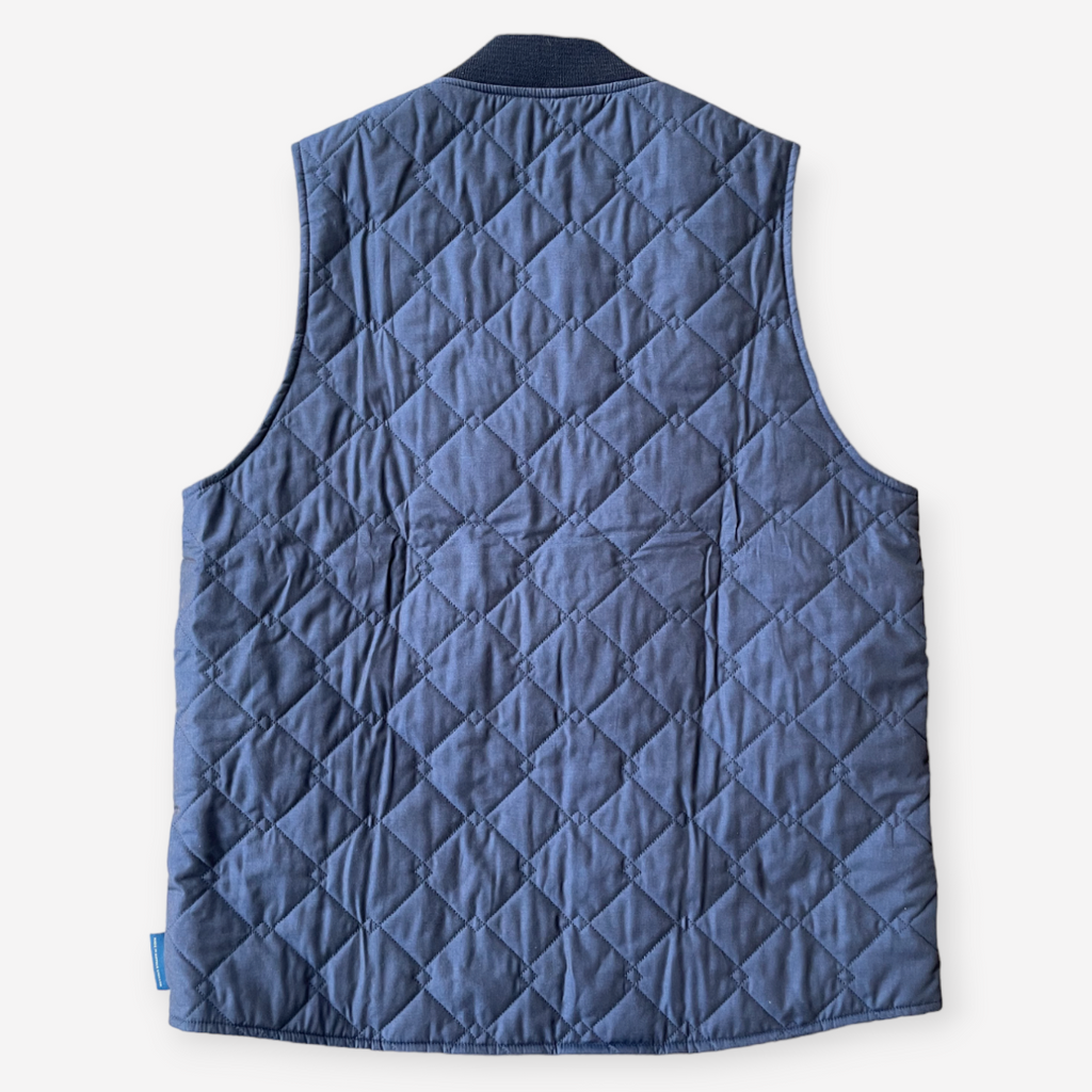 A navy quilted bomber gilet with a zip fastening, ribbed collar, cross diamond pattern, large welt pockets, and lightweight cotton fabric.