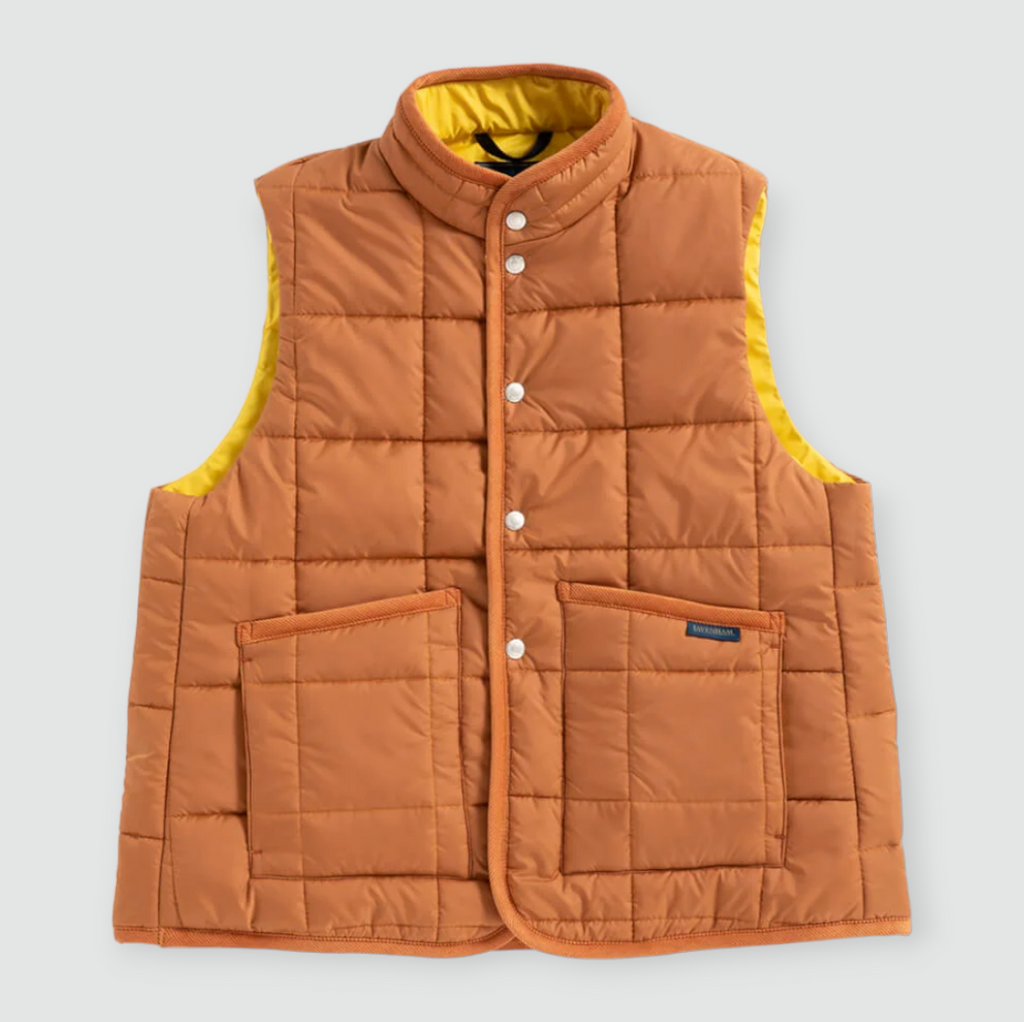 A brick-colored quilted gilet with stand collar, patch pockets, and organic cotton corduroy binding, made from recycled polyester and technical wadding.