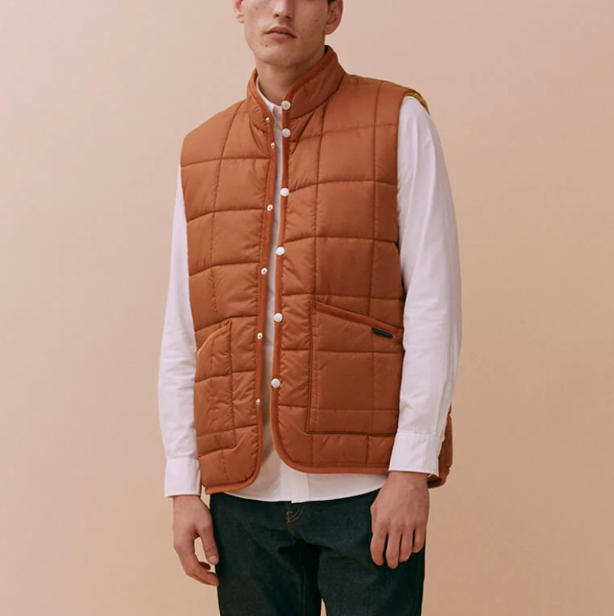 A brick-colored quilted gilet with stand collar, patch pockets, and organic cotton corduroy binding, made from recycled polyester and technical wadding.